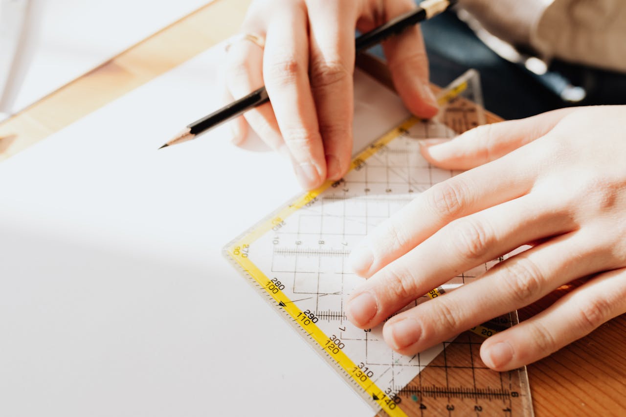 Hands using a ruler and pencil for precise drawings on white paper.